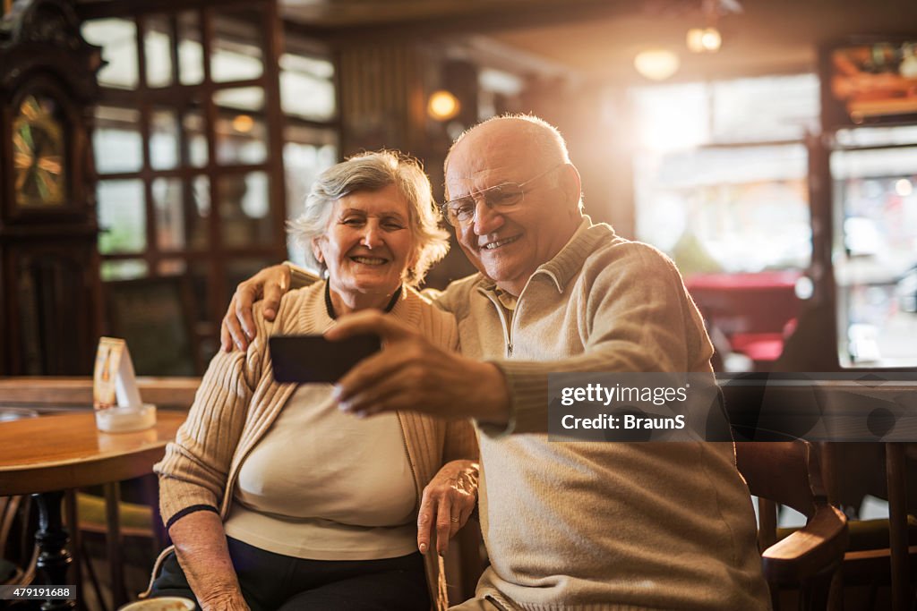 Embraced old couple taking a selfie with cell phone.