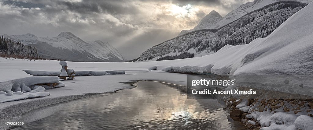 Reflection of sunrise and mountains in snowy pond