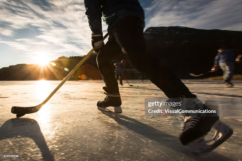 Playing ice hockey on frozen lake in sunset.