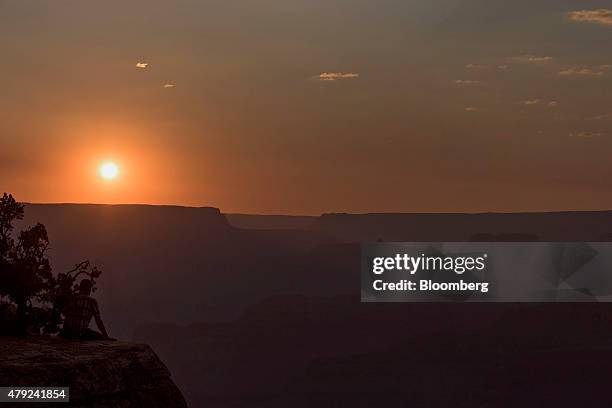 Visitor sits on a ledge while watching the sun set from Hopi Point at Grand Canyon National Park in Grand Canyon, Arizona, U.S., on Wednesday, June...