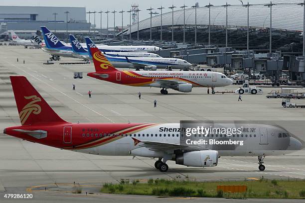 All Nippon Airways Corp. , top, and Hong Kong Airlines Ltd., center, aircrafts sit parked as a Shenzhen Airlines Co. Aircraft taxies at the Kansai...