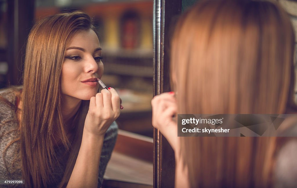Reflection in mirror of a beautiful woman applying lipstick.