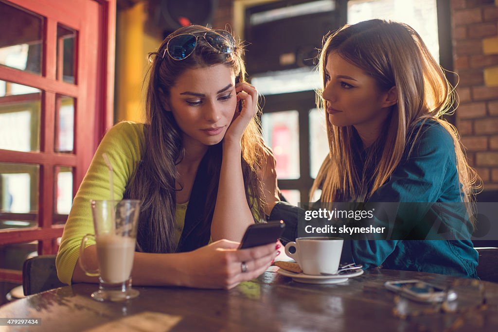 Sad woman reading text message to her friend in cafe.