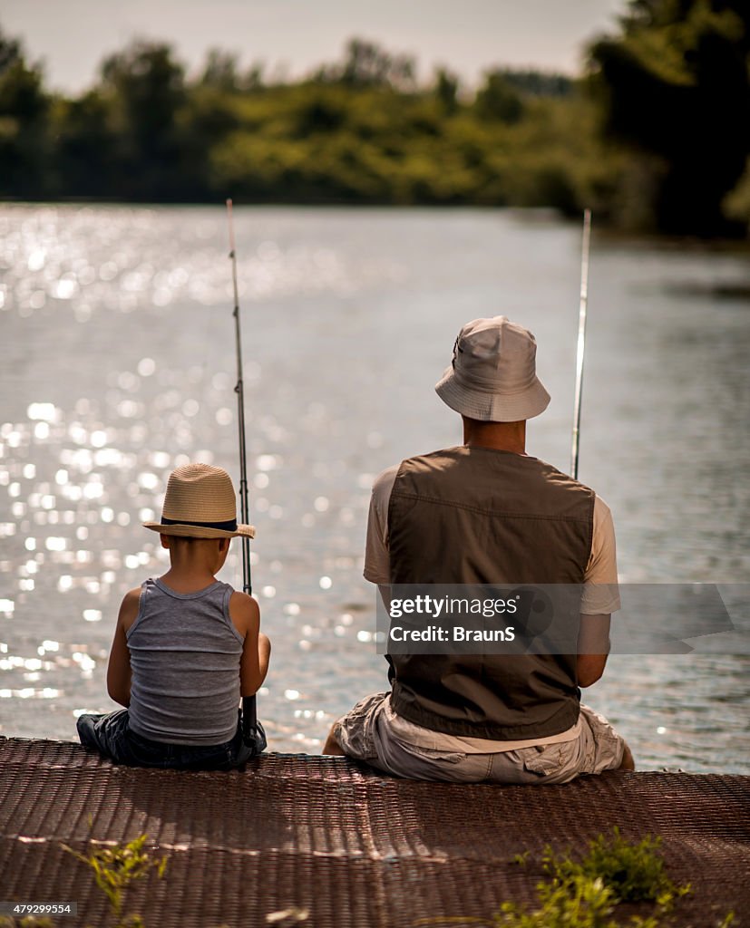Rear view of a father and son fishing from pier.