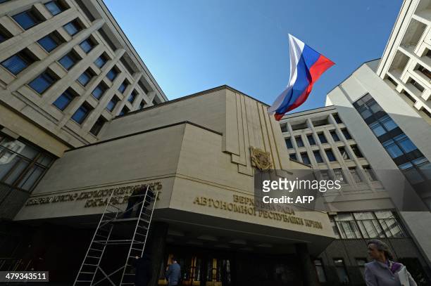 Russian flag waves in the courtyard of the parliament building in Simferopol, Crimea, on March 18 while workers dismantled the inscription reading...
