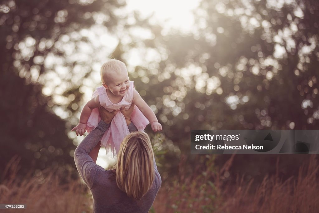 Mother lifting laughing baby girl over her head