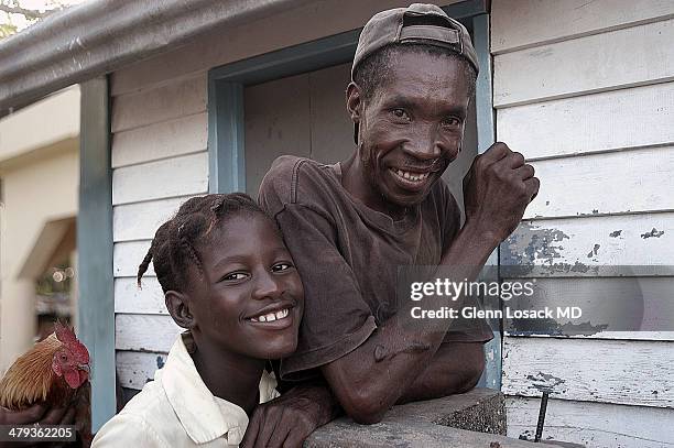 Father his son stand in front of their shack. A rooster is in the background they are smiling father has a keloid Santa fe San Pedro Dominican...