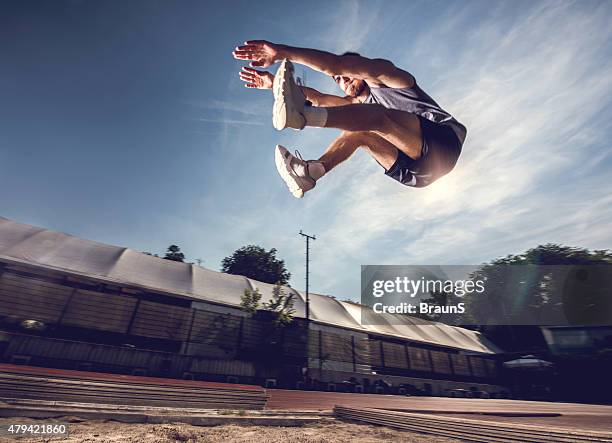 below view of a young athlete in a long jump. - verspringen stockfoto's en -beelden