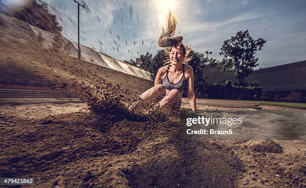 young female athlete landing in sand after a long jump. - verspringen stockfoto's en -beelden