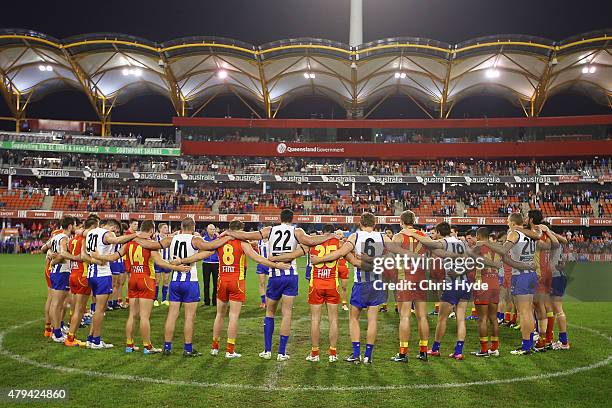 Both sides huddle in the middle of the ground to pay respect to Phil Walsh during the round 14 AFL match between the Gold Coast Suns and the North...