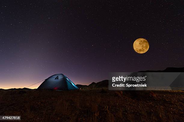 full red moon and stars over lit tent in desert - camping at night stockfoto's en -beelden