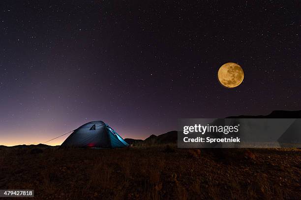 full red moon and stars over lit tent in desert - full moon stock pictures, royalty-free photos & images