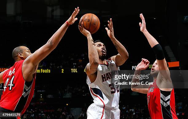 Mike Scott of the Atlanta Hawks shoots against Chuck Hayes and Jonas Valanciunas of the Toronto Raptors at Philips Arena on March 18, 2014 in...