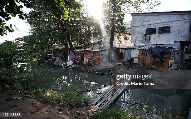 Resident walks over a makeshift bridge above a polluted stream in an impoverished area in the unpacified Complexo da Mare slum complex, one of the...