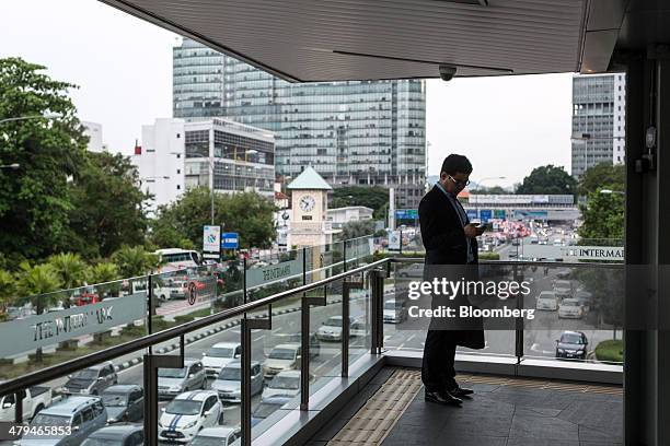 An office worker checks his mobile phone while standing on a walkway in Kuala Lumpur, Malaysia, on Tuesday, March 18, 2014. Malaysia, aspiring to...