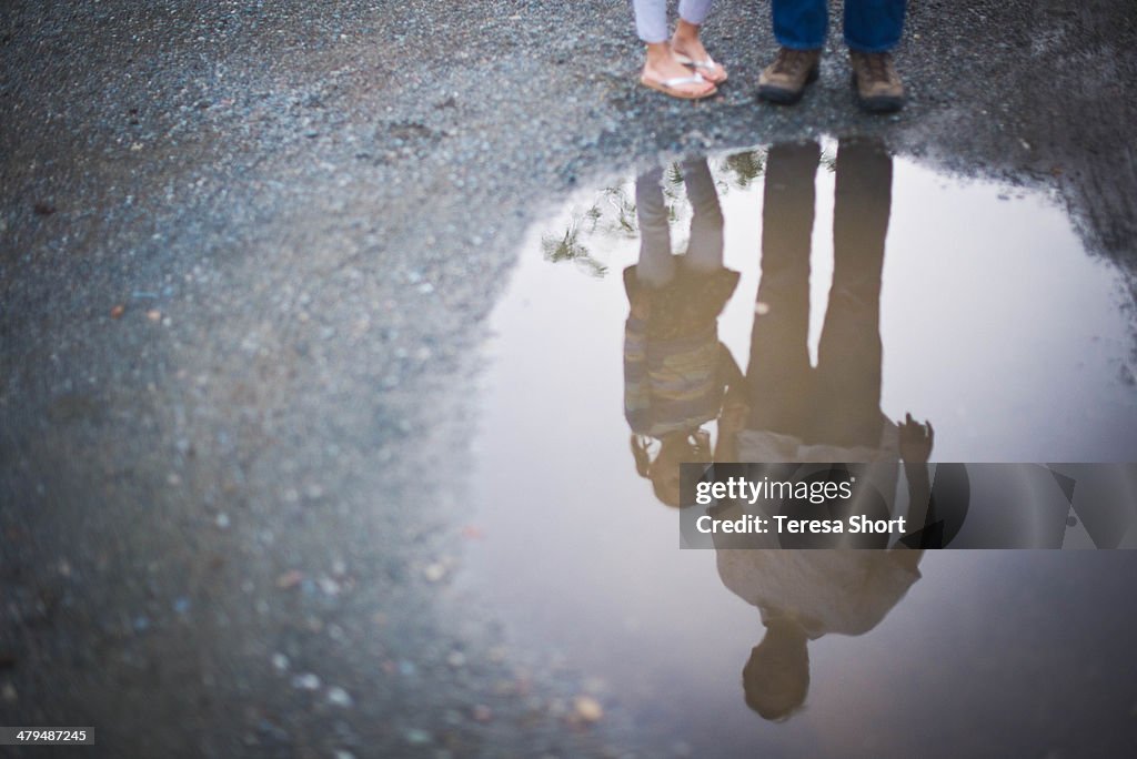 Father and Daughter stand in Puddle Reflection