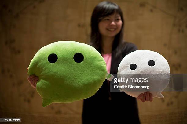 Woman poses for a photograph with WeChat pillows promoting Tencent Holdings Ltd. Free message applications ahead of the company's news conference in...