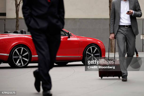 Businessmen walk past a Bentley Continental GT convertible automobile, produced by Bentley Motors Ltd., following a news conference to announce the...