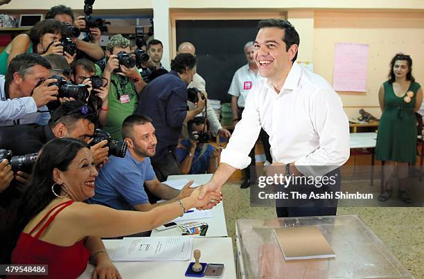 Greek Prime Minister Alexis Tsipras shakes hands with voting station staff after casting his referendum vote at a school in the suburbs of Athens on...