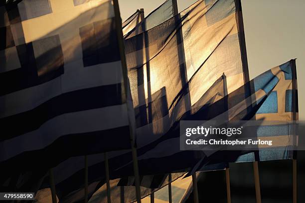 The sun sets through Grrek flags over the Greek parliament as the polls have now closed in the Greek austerity referendum and people are begining to...