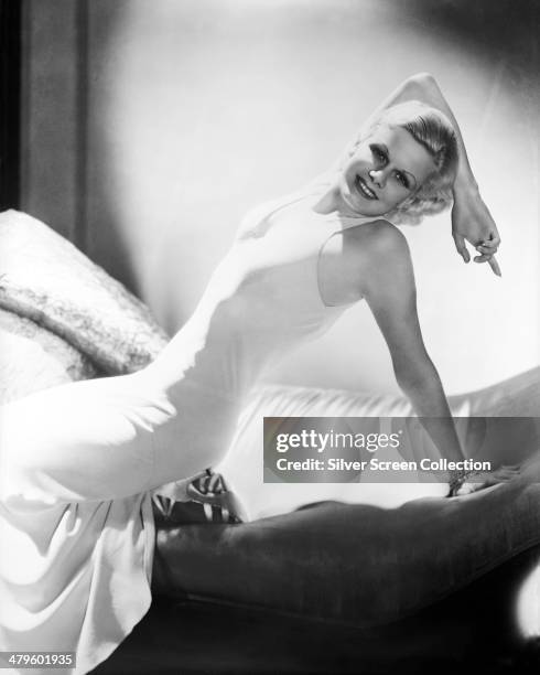 American actress Jean Harlow posing on a chaise longue in a white, sleeveless dress, circa 1932.