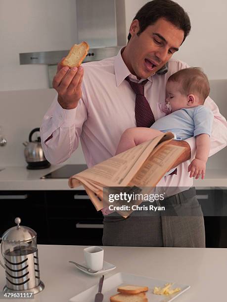 father talking on phone with toast while holding baby daughter in a kitchen - stress eating stock pictures, royalty-free photos & images