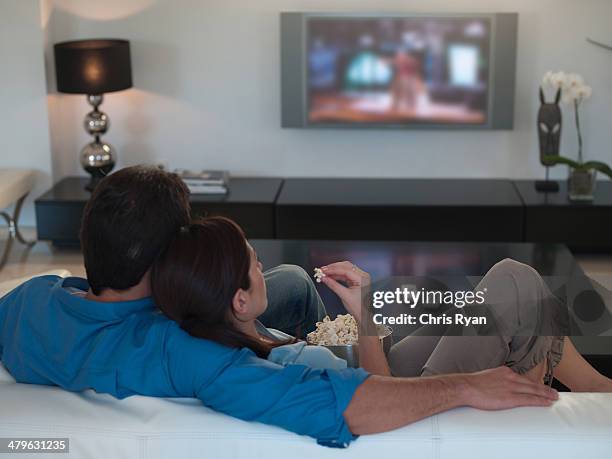 couple watching television together and eating popcorn - movie date night at home stock pictures, royalty-free photos & images