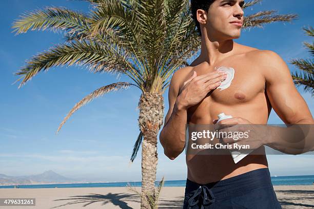 man on a beach applying sunblock lotion to himself - running shorts stock pictures, royalty-free photos & images