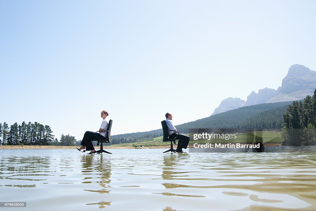 Businessman and woman in office chairs on water facing away
