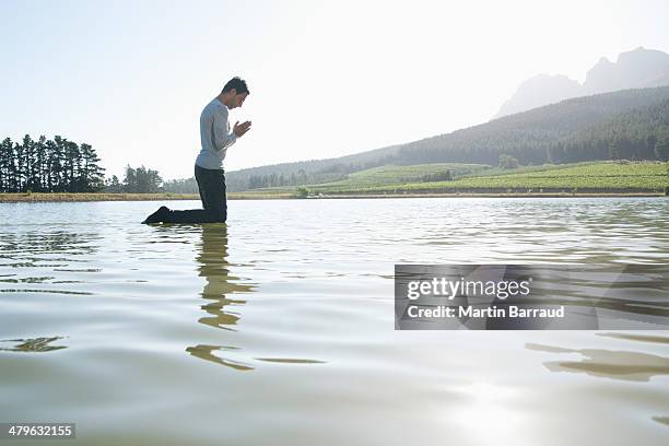 man kneeling on water praying - holy baptism stock pictures, royalty-free photos & images