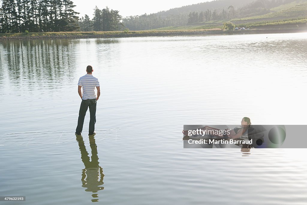 Woman lying on flotation device and man standing on water 