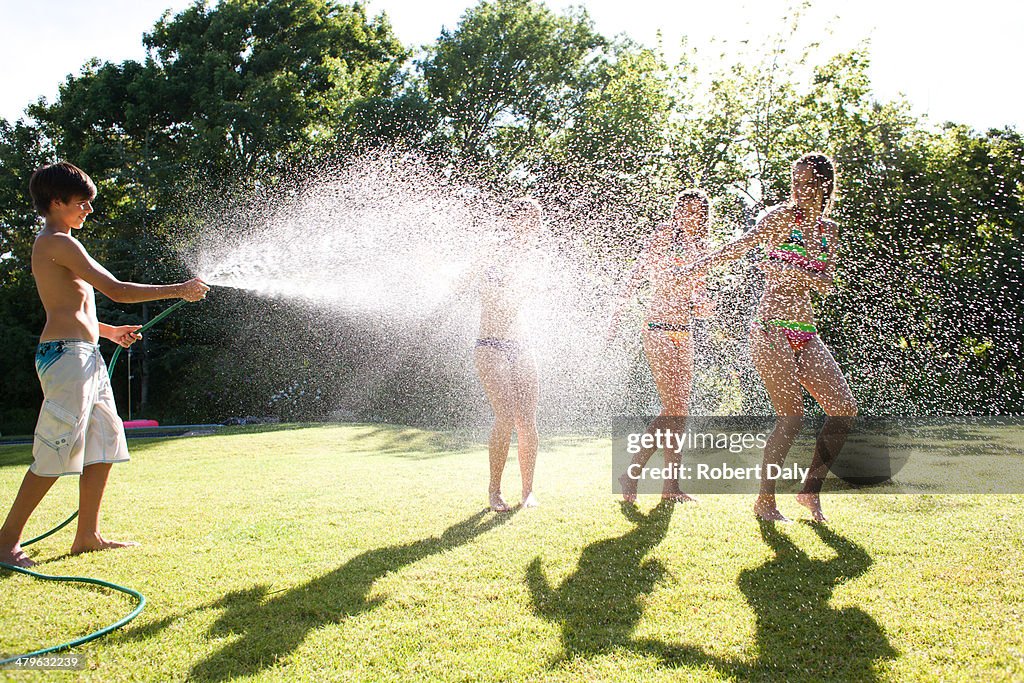 Teenage boy spraying teenage girls with hose outdoors