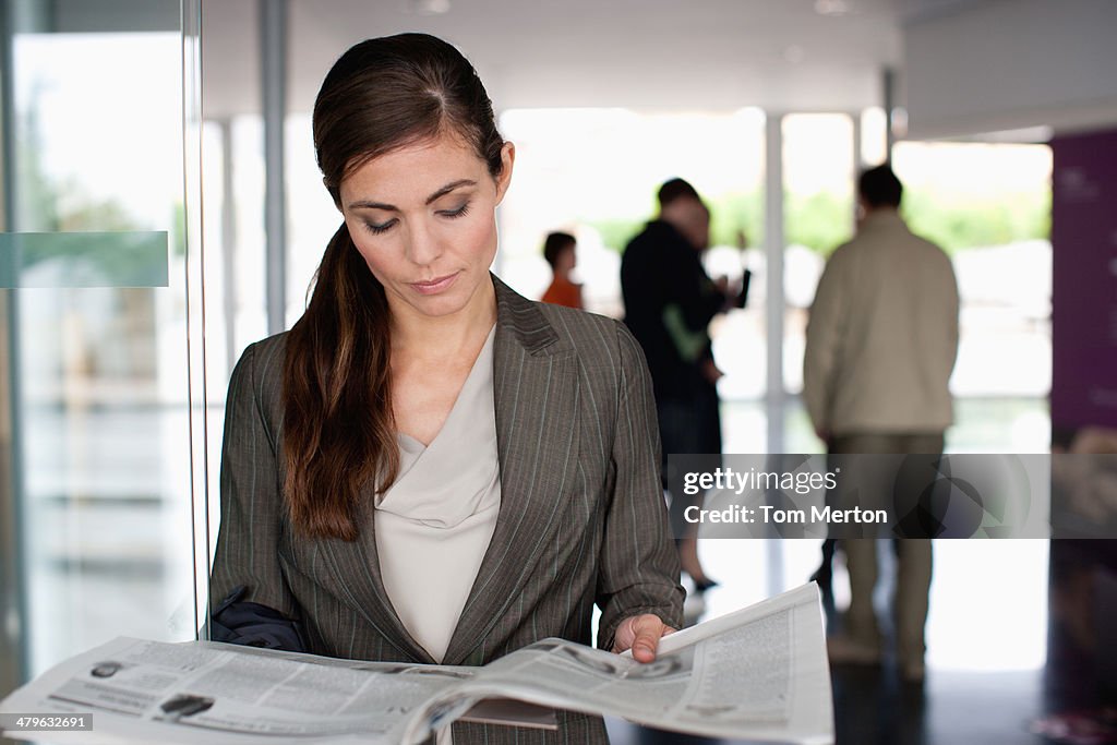 Businesswoman reading newspaper in office lobby