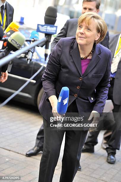 German Chancellor Angela Merkel picks up a reporter's microphone that fell to the ground upon her arrival at the EU headquarters in Brussels on March...