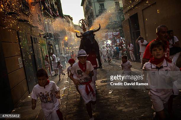 Revellers and children are 'chased' by the 'Toro de Fuego' as it runs throught the streets during the opening day of the San Fermin Running of the...