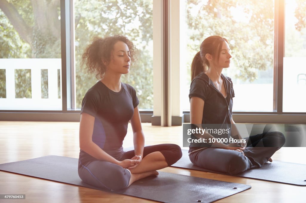 Two women sitting in a yoga class meditating