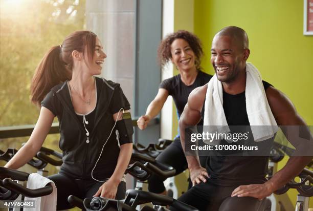 one man, two woman smiling on exercise bike in a g - trainingsmaschine stock-fotos und bilder