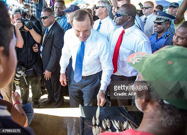 Australian Prime Minister Tony Abbott picks up a fish from a stall during his tour of a market in Port Moresby on March 21, 2014. Abbott arrived here...