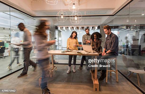 young colleagues using laptop in the office among blurred people. - group people thinking stock pictures, royalty-free photos & images