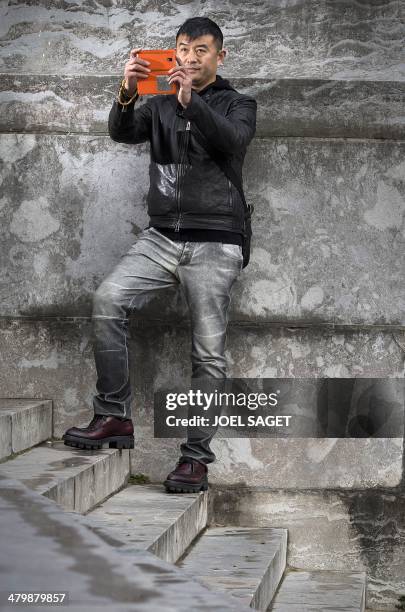 Chinese artist Liu Bolin takes pictures with a mobile phone during the installation of his art creation, a giant fist sculpture "Iron First", at the...