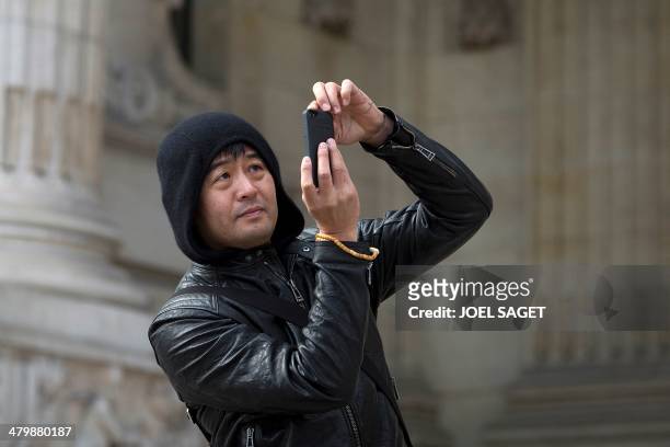 Chinese artist Liu Bolin takes pictures with a mobile phone during the installation of his art creation, a giant fist sculpture "Iron First", at the...