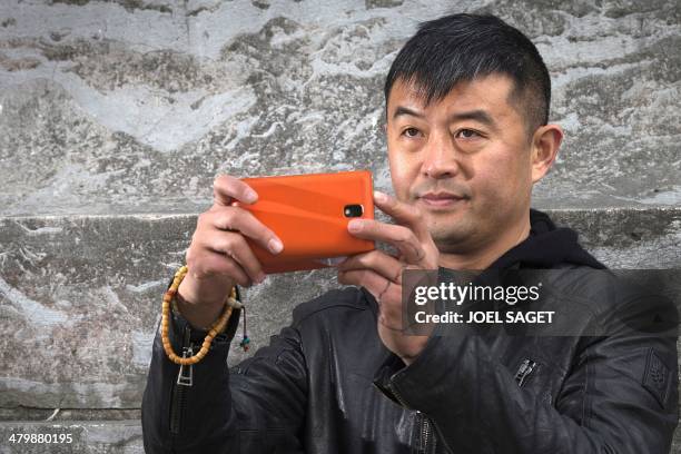 Chinese artist Liu Bolin takes pictures with a mobile phone during the installation of his art creation, a giant fist sculpture "Iron First", at the...