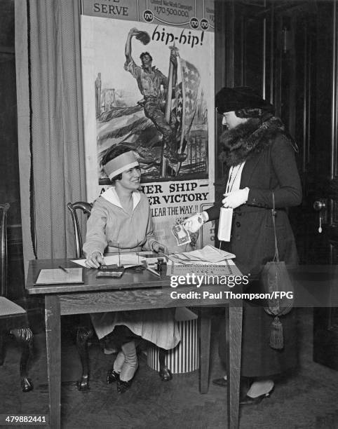Mrs Edward C. Ely makes a purchase from Miss Joyce Shaw Kennedy at the Red Cross Shop, USA, during World War I, 1918. The poster behind them is by...