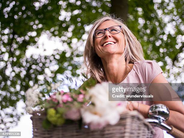 mature woman smiling while cycling under trees - bicycle flowers stockfoto's en -beelden