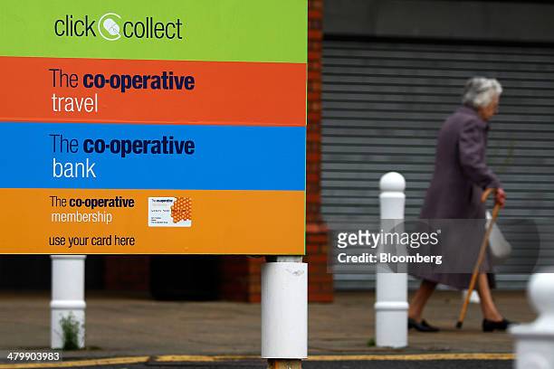 An elderly lady walks with a walking stick as she passes signs for services offered by the Co-Operative Group Ltd., including 'click and collect'...