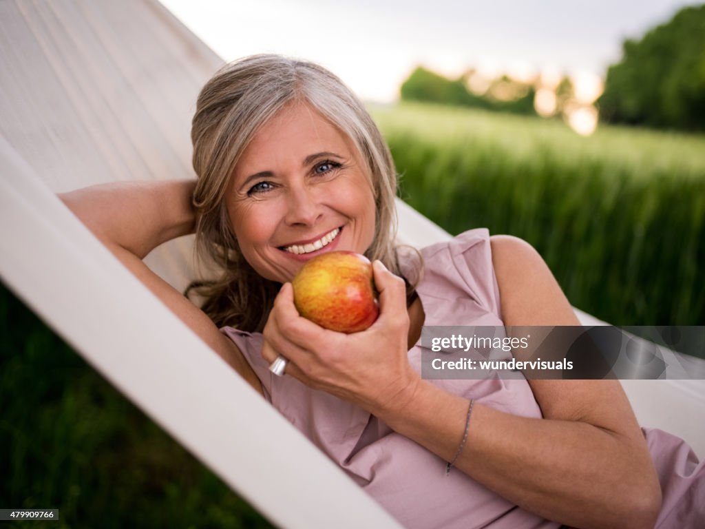 Mature woman eating a fresh apple while relaxing outdoors