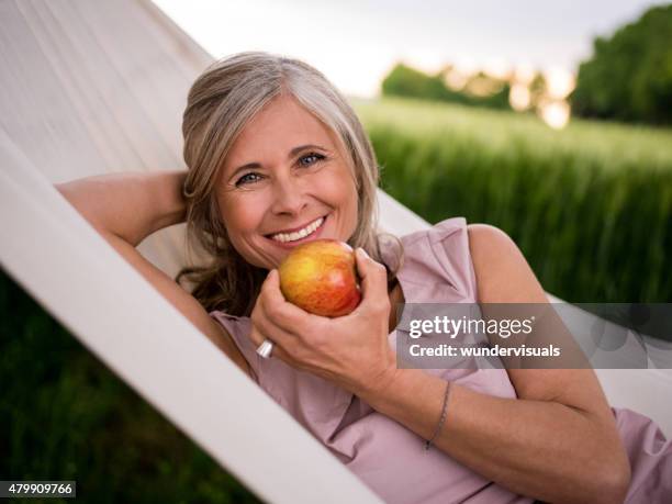 mature woman eating a fresh apple while relaxing outdoors - ripe stock pictures, royalty-free photos & images