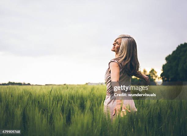 mature woman feeling youthful in a lush summer field - alleen oudere vrouwen stockfoto's en -beelden