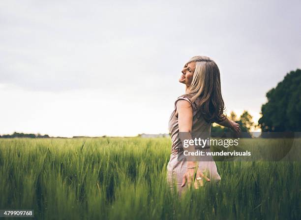 mature woman feeling youthful in a lush summer field - woman on walking in countryside stock pictures, royalty-free photos & images