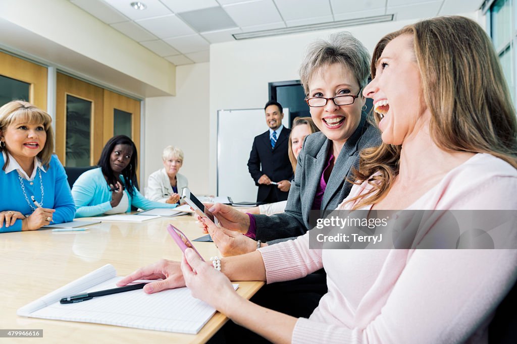 Two Women Laugh at Cell Phone Images at Business Meeting